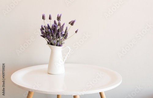 Purple lavender in small white jug on round table against neutral wall