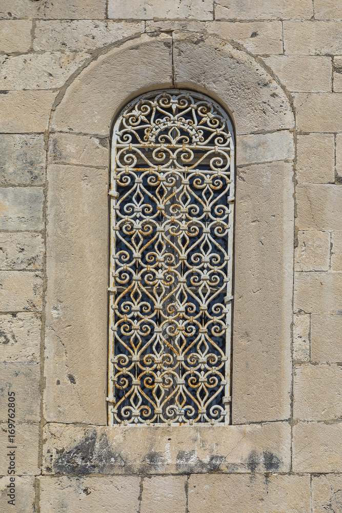 окно в каменной стене с кованной решеткой 