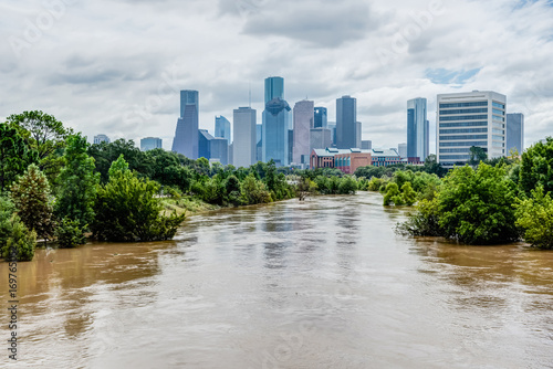 High and fast water rising in Bayou River with downtown Houston in background under cloud blue sky. Heavy rains from Harvey Tropical Hurricane storm caused many flooded areas in greater Houston area. photo