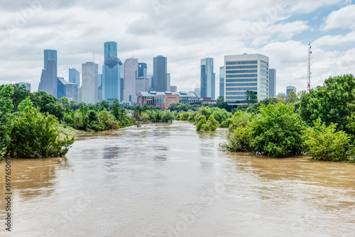 Valokuva High and fast water rising in Bayou River with downtown Houston in background under cloud blue sky