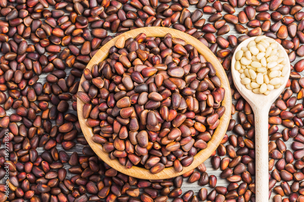 Fototapeta premium Unpeeled pine nuts in a wooden bowl on wooden background. Top view.