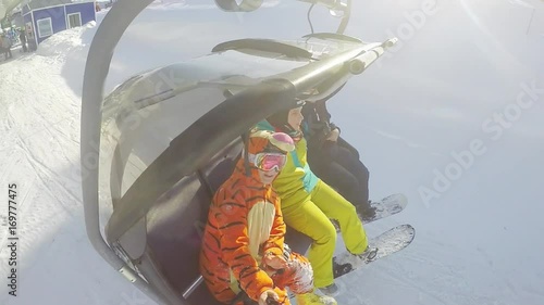 Friends snowboarders riding up ski lift in sunny winter day through the ssun with lens flare effects in slow motion. 1920x1080 photo