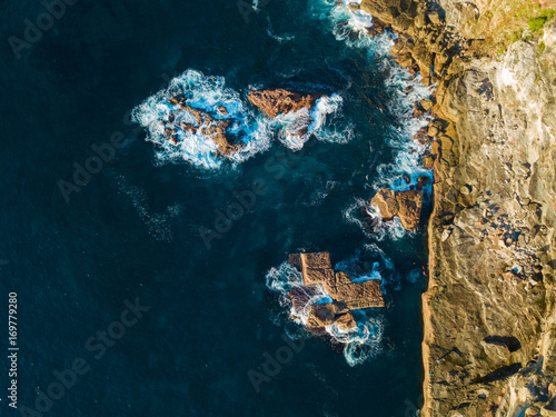 Aerial view of rock cliff and four rocks beside it on the ocean.