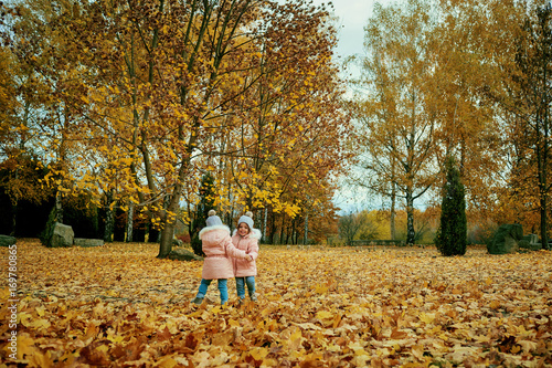 Two happy children playing in autumn clothes in the park. Little sister girls sitting on yellow leaves in nature. © Studio Romantic