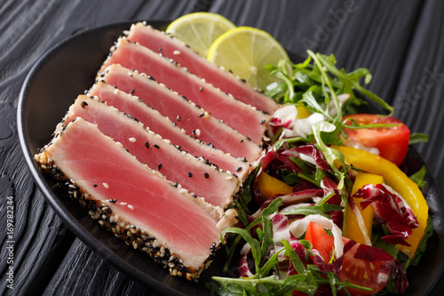Delicious Tuna Steak in sesame, lime and salad of fresh vegetables and herbs close-up. horizontal