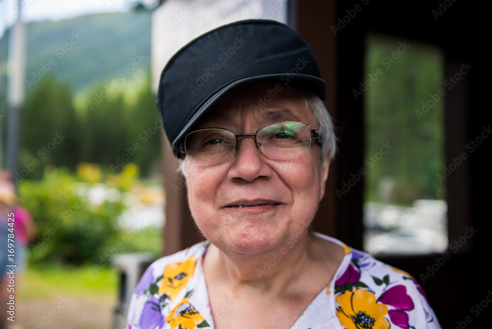 Happy healthy smiling old lady portrait wearing blue cap and glasses outdoor