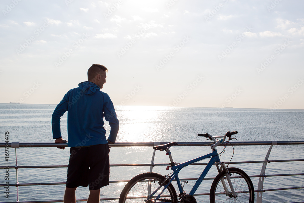 Young man with bicycle in the morning, sunrise in the sea background 