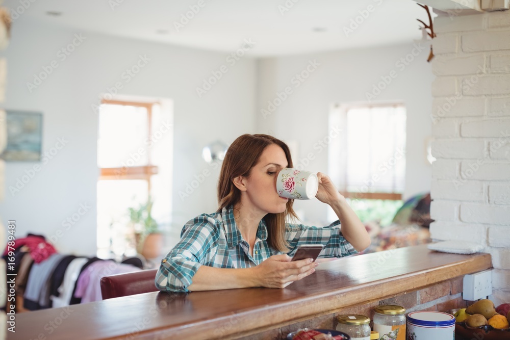 Woman using mobile phone while having coffee in kitchen Woman using mobile phone while having coffee in kitchen