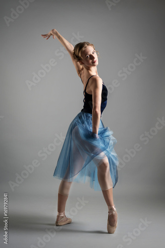 beautiful girl ballerina dancing in a lush blue skirt on grey background in Studio