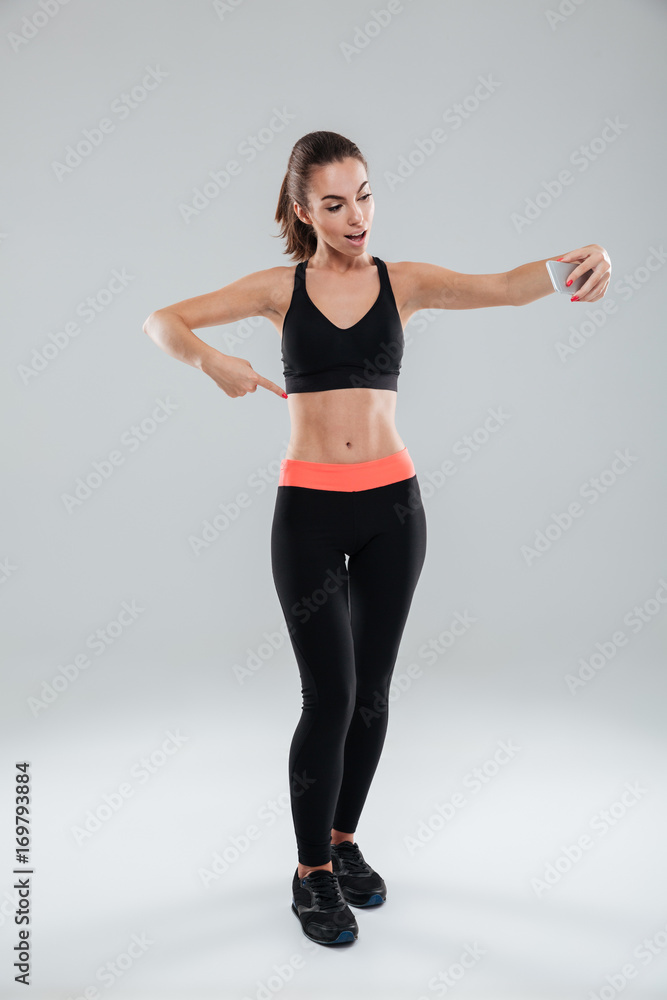 Full length picture of happy fitness woman pointing at abdominals