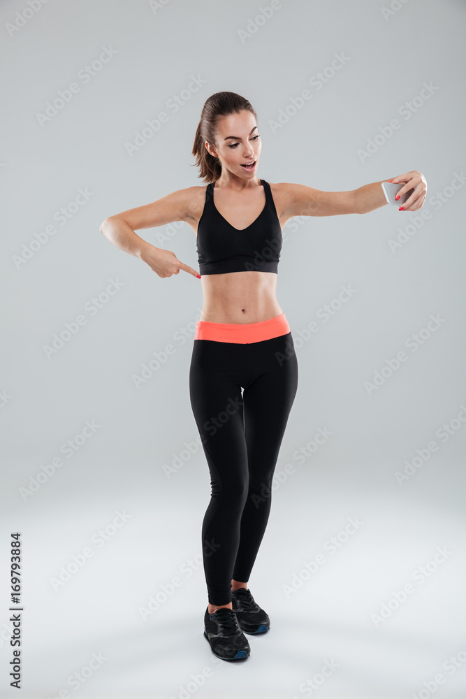 Full length picture of happy fitness woman pointing at abdominals Full length picture of happy fitness woman pointing at abdominals