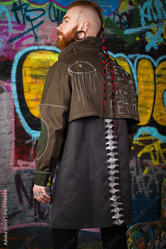Obraz premium A creative, unusual red-haired man in designer clothes and tunnels in his ears, posing in the studio.
