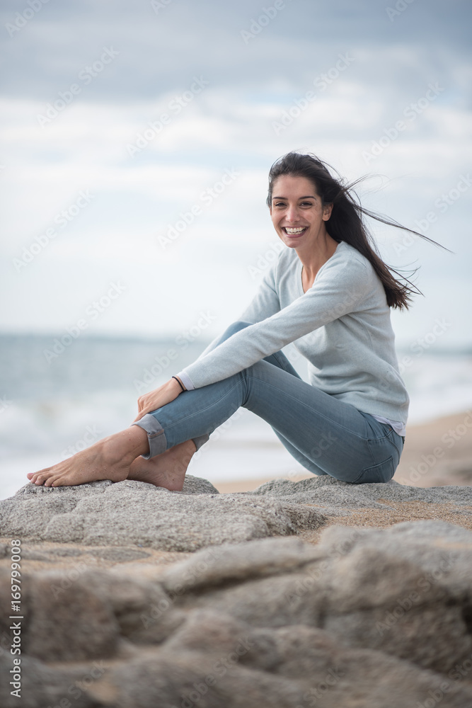 A beautiful young brunette sitting on a rock at the beach