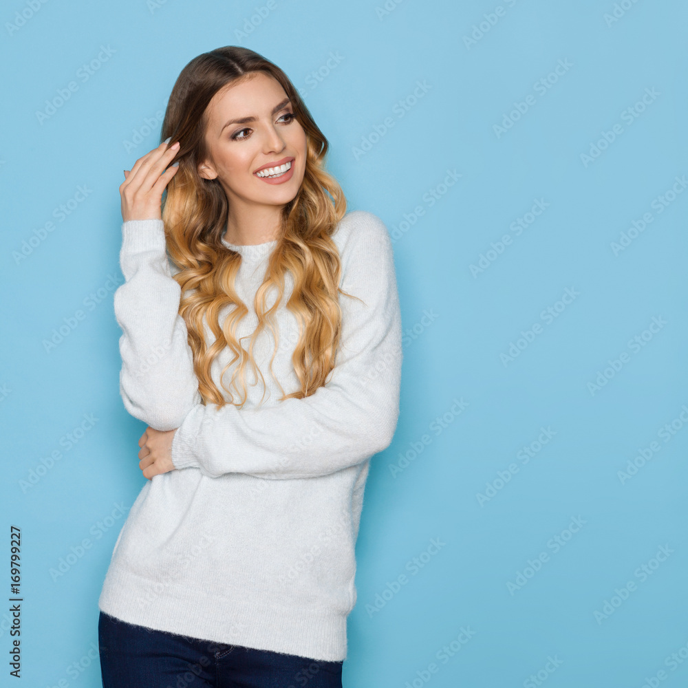 Smiling Beautiful Young Blond Woman In Pastel Blue Sweater And Jeans Is Looking Away Smiling Beautiful Young Blond Woman In Pastel Blue Sweater And Jeans Is Looking Away