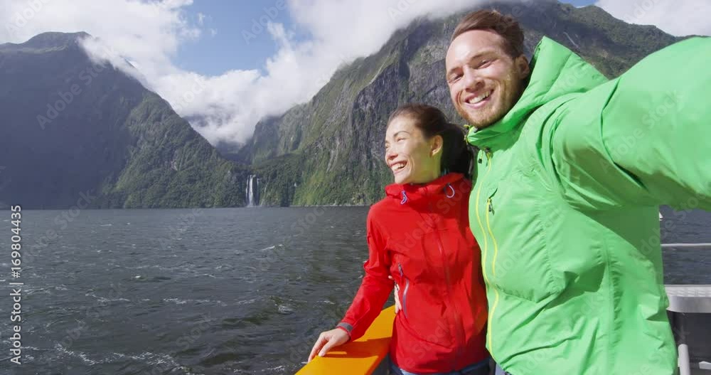 Couple taking selfie video using smart phone on cruise ship, Milford Sound, Fiordland National Park, New Zealand. Multicultural couple smilng having fun laughing on travel vacation. SLOW MOTION. Couple taking selfie video using smart phone on cruise ship, Milford Sound, Fiordland National Park, New Zealand. Multicultural couple smilng having fun laughing on travel vacation. SLOW MOTION.