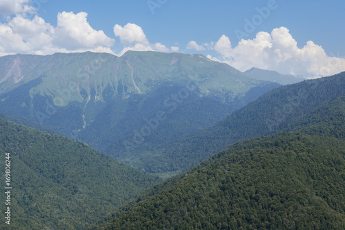 The mountains are covered with dense green forest on blue sky background