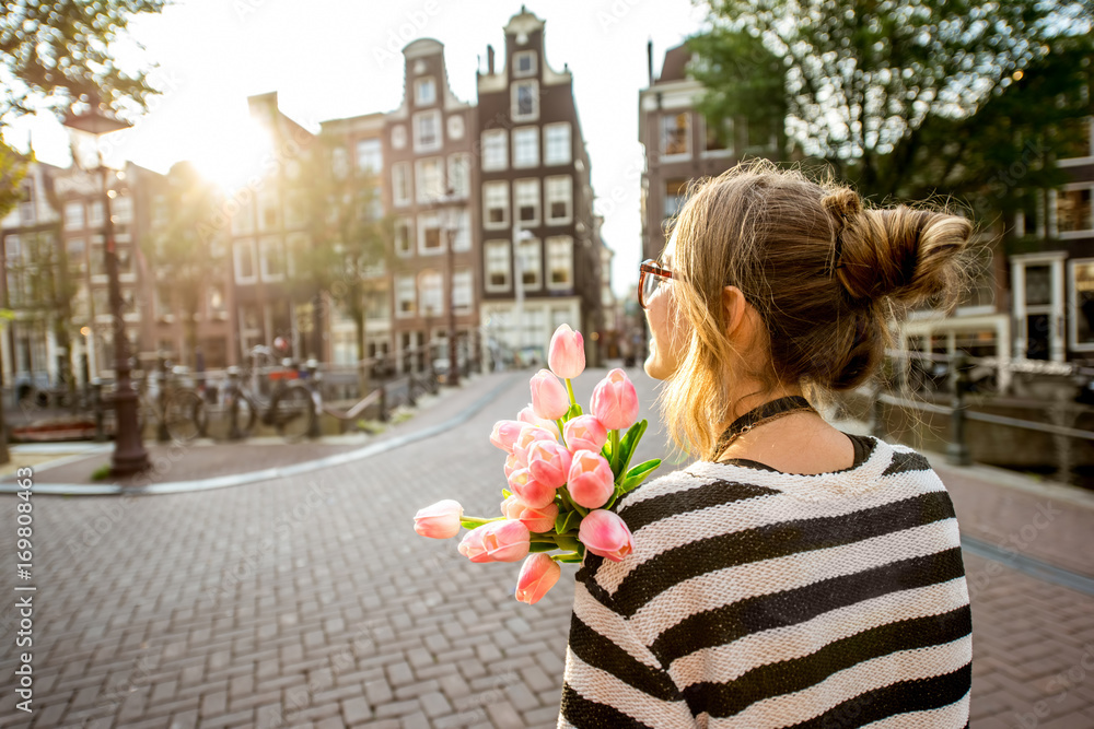 Fototapeta premium Woman enjoying great view on the buildings holding a bouquet of pink tulips in Amsterdam city