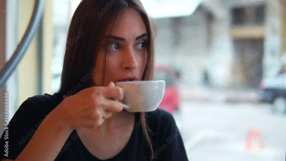 Closeup view of attractive young woman dreaming with cup of hot coffee sitting by the window in the coffee shop. Break after long busy day. Relaxation with a warm cup of tea Closeup view of attractive young woman dreaming with cup of hot coffee sitting by the window in the coffee shop. Break after long busy day. Relaxation with a warm cup of tea