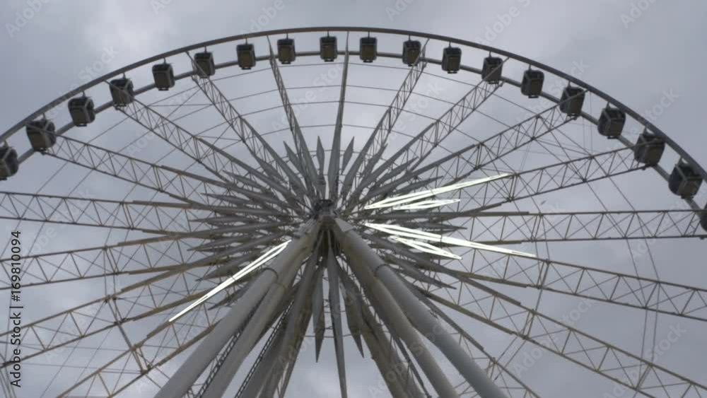A giant Ferris wheel with flashing lights spins in front of a dull grey sky. Low angle. A giant Ferris wheel with flashing lights spins in front of a dull grey sky. Low angle.