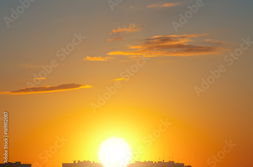 A huge sun sets over the roofs of houses in the city.