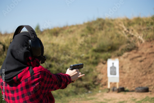 A young girl holds a pistol and targets a shot at a shotgun, headphones on the head, a big burst of a pistol, a young cop