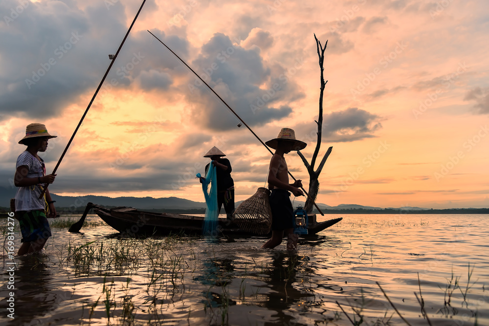 Asian fisherman on wooden boat casting a net for catching freshwater fish  in nature river in the early morning before sunrise Stock Photo