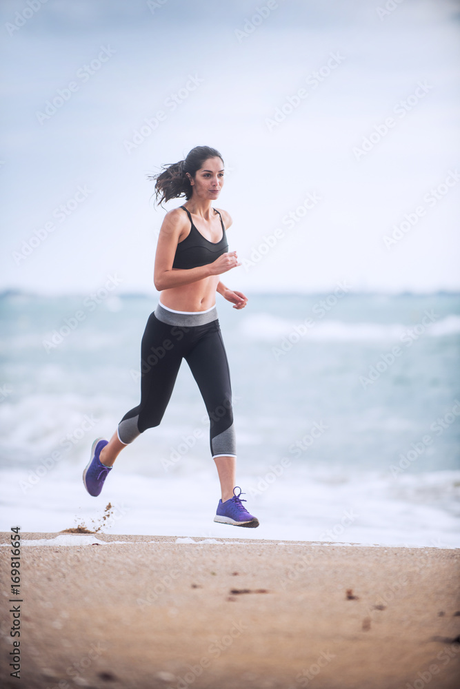 Beautiful young woman in sportswear runs on the beach