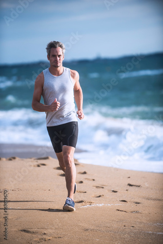 Gray haired man in sportswear runs on the beach