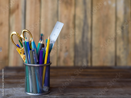 Colorful pencils of violet yellow gray green and blue in stationary cup on wooden table and background. Copyspace school concept