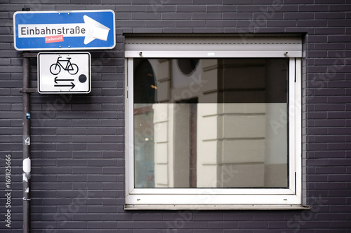 Einbahnstraßenschild an Hausecke / Ein senkrecht stehendes Einbahnstraßenschild an der Ecke eines geklinkerten Wohngebäudes mit einem Fenster.