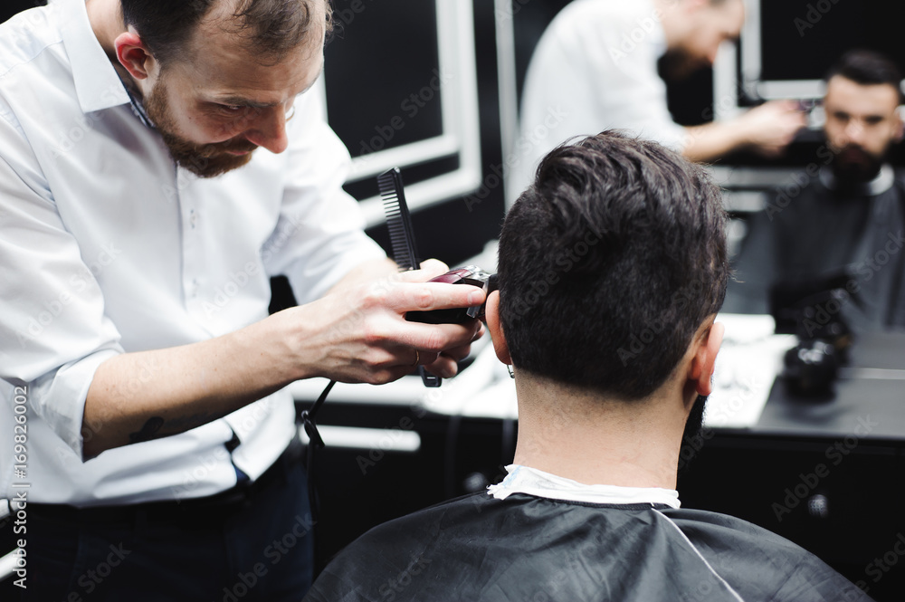 Fototapeta premium Master cuts hair and beard of men in the barbershop, hairdresser makes hairstyle for a young man