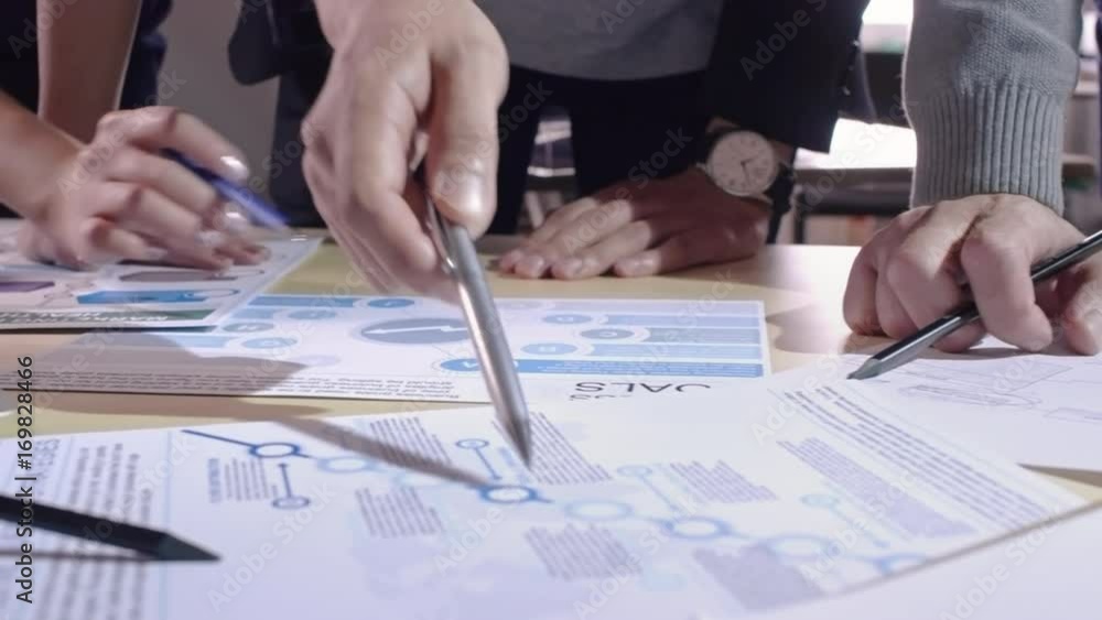 Tracking shot of hands of businessmen and businesswomen pointing with pens at schemes on documents while planning company goals and strategy at meeting Tracking shot of hands of businessmen and businesswomen pointing with pens at schemes on documents while planning company goals and strategy at meeting