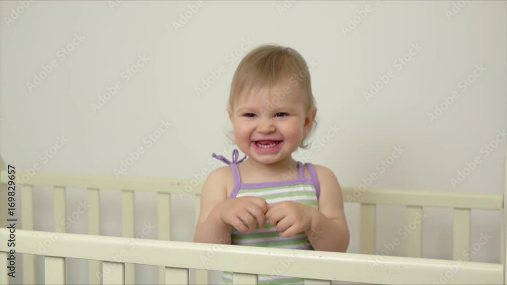 Cute little girl standing on a bed laughing happily and clapping her hands Cute little girl standing on a bed laughing happily and clapping her hands