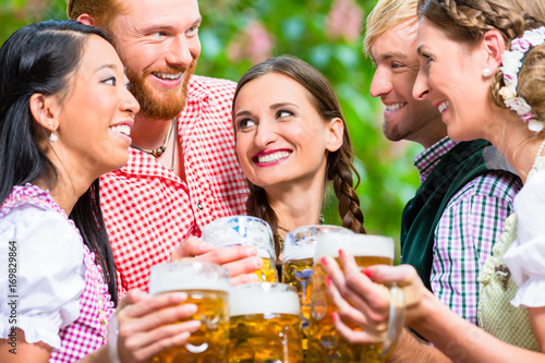 Freunde, zwei Männer, drei Frauen, stehen im Biergarten mit Maßkrügen