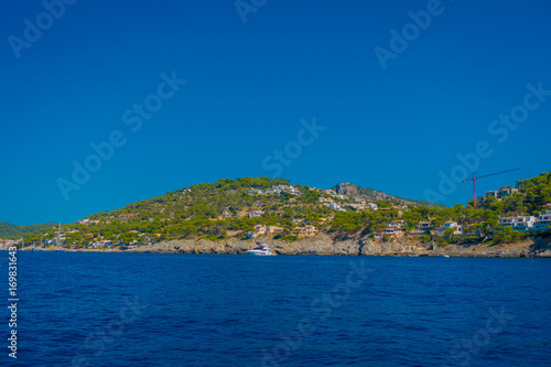 Beautiful view of Mallorca balearic islands, with some buildings in the mountain in the horizon, with gorgeous blue water and a beautiful blue sky, in Spain