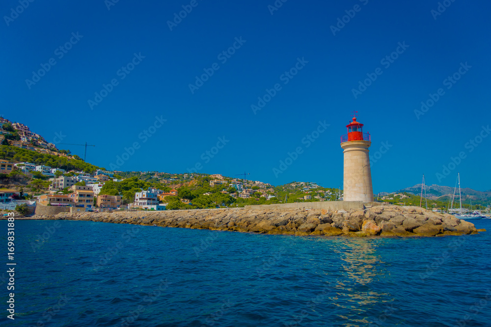 Beautiful view of Mallorca balearic islands, with a lighthouse and some buildings in the mountain in the horizon, with gorgeous blue water and a beautiful blue sky, in Spain