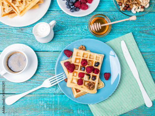 Homemade waffles with raspberries and blueberry, cup of coffee, milk and cutlery photo