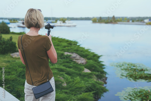 Woman filming with small personal camera a park with a river