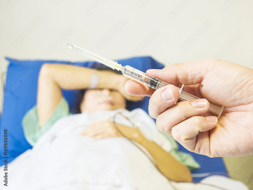 Doctor holding syringe in hand ready for injecting with a patient background in the hospital Doctor holding syringe in hand ready for injecting with a patient background in the hospital
