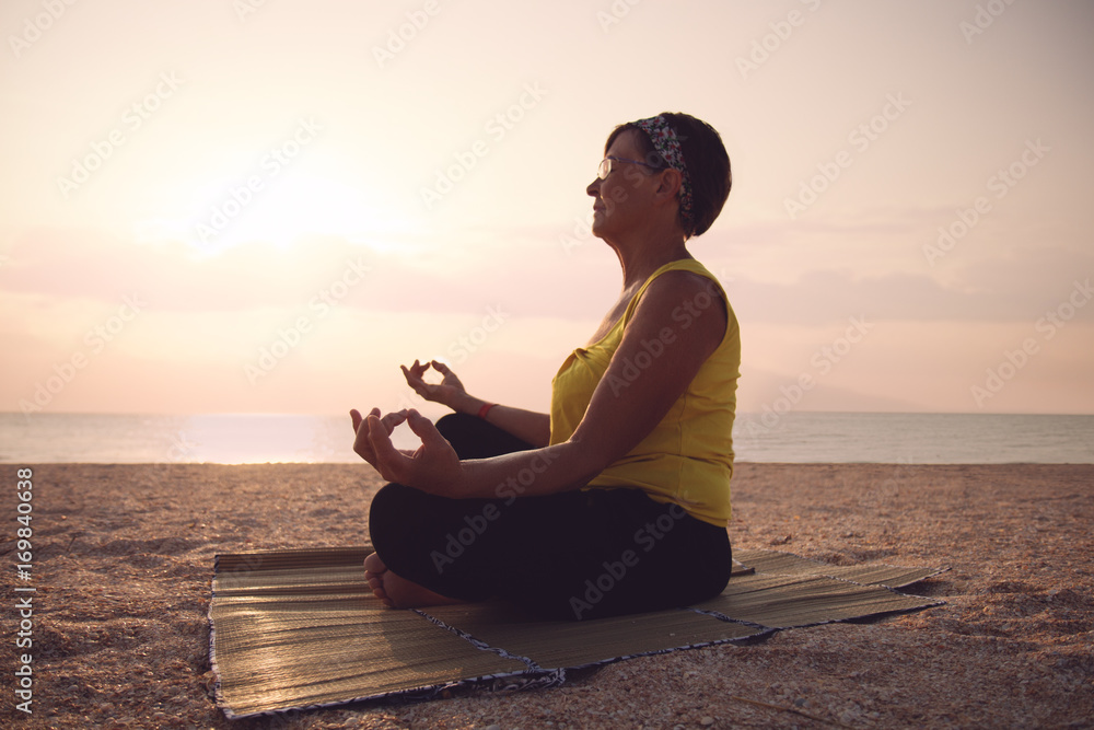 Mature woman practicing yoga at lotus pose, at the sea beach