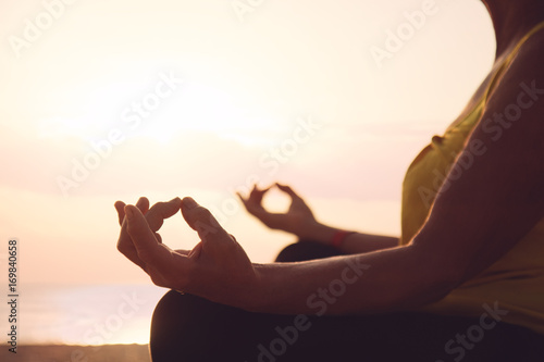 Hands of mature woman practicing yoga at lotus pose, at the sea beach
