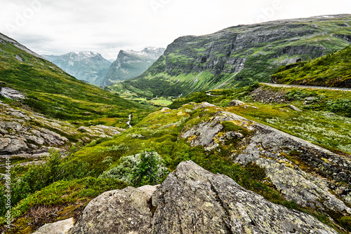 Path over green pasture in the mountains of Western Norway with snow on the summits and a dark cloudy sky