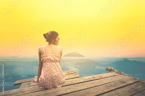 Young woman sitting on wood pier looking mountain landscape view.