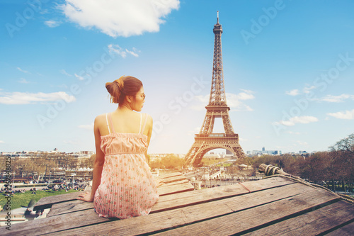 Young woman sitting on wood pier looking Eiffel tower, back view. © Khritthithat