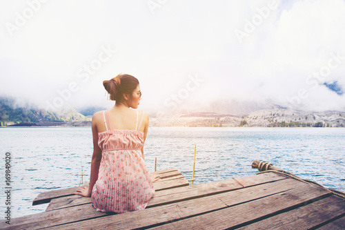 Young woman sitting on wood pier looking in the sea, back view.