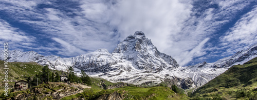 Panoramic view of the south face of the Matterhorn, view from the Breuil-Cervinia village.Green meadow in the front and blue sky with white clouds above mountains. Summer in the Alps, Italy, Europe.