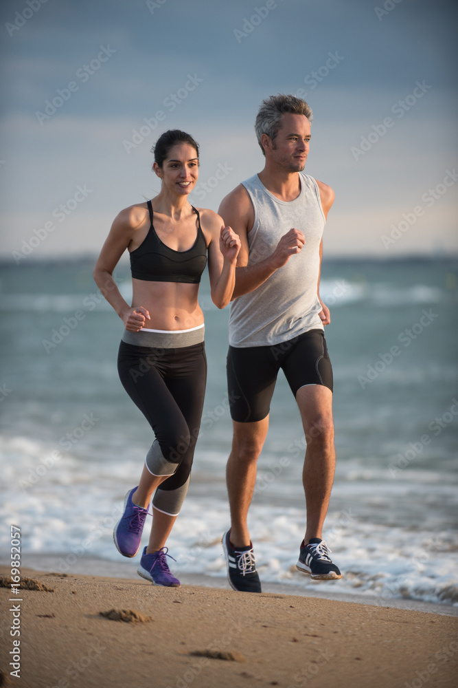A couple wearing sportswear is running on the beach A couple wearing sportswear is running on the beach