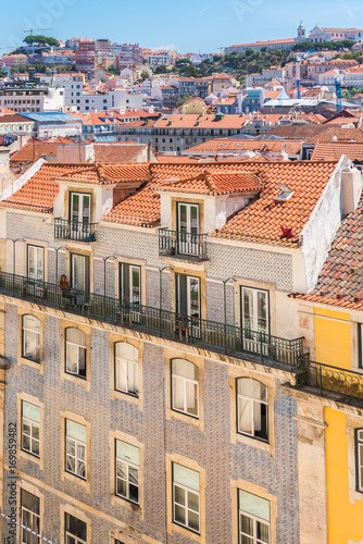      Orange tiles roofs in lisbon, Portugal, typical houses, woman on a balcony
