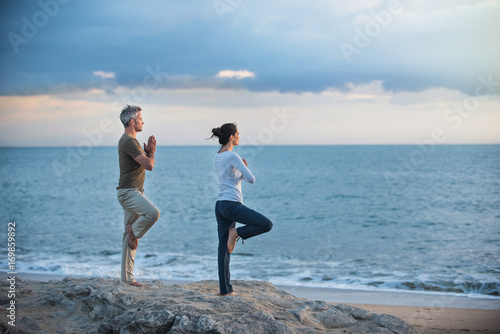 Beautiful couple practicing yoga on the beach at sunrise photo