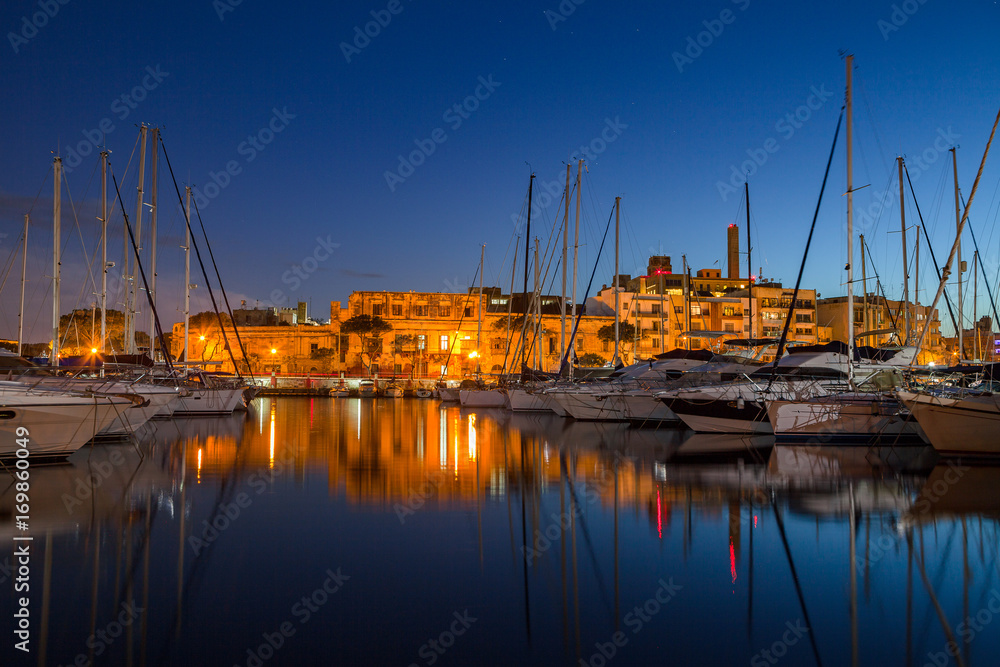Night view of marina with sail boats and yachts and illuminated architecture. Malta island.